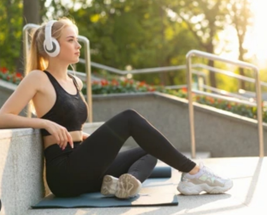 A woman sitting on stairs while listening to music on her headphones after yoga session.